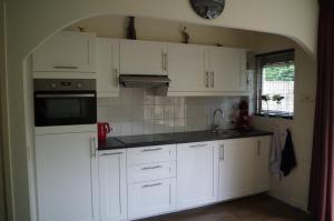a kitchen with white cabinets and a sink at Geschakelde bungalow op de Veluwe "De Eekhoorn" in Otterlo +15 photos