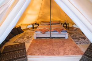 a bed in a tent with two tables and two rugs at Natur Camp Birštonas in Birštonas