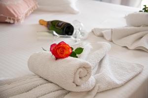 Nausika Cottage Corfu في باليوكاستريتسا: منشفة مع وردة على السرير مع زجاجة من النبيذ