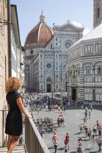 Eine Frau steht auf einem Balkon mit Blick auf ein großes Gebäude in der Unterkunft Luxury Bed and Breakfast Cerretani Palace in Florenz