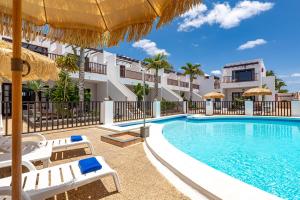 a swimming pool with chairs and umbrellas next to a building at Apartamentos las Lilas in Puerto del Carmen