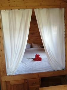 a bed with white curtains and a red flower on it at Roulotte et Jacuzzi de Rachel au Domaine du Reuze in Winnezeele