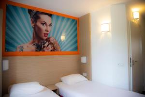 - 2 lits dans une pièce avec une photo de femme dans l'établissement Kyriad Direct Arras - Saint-Laurent-Blangy - Parc Expo, à Saint-Laurent-Blangy