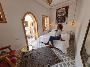 Riad Le Petit Joyau في مراكش: امرأة تجلس على سرير في غرفة