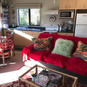 a living room with a red couch in a kitchen at Pet Friendly Country Cottage in Dunedin