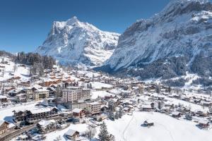 a town covered in snow with a mountain in the background at Belvedere Swiss Quality Hotel in Grindelwald