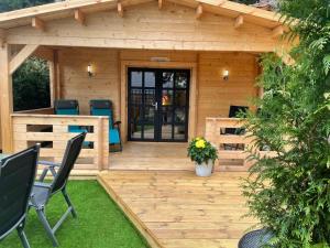 a wooden cabin with a deck with chairs on it at O Dan Y Coed Swedish Log Cabin with New 2024 Wood Fired Hot Tub in Chwilog