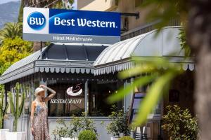 a woman standing in front of a restaurant sign at Best Western Hotel Mediterranee Menton in Menton