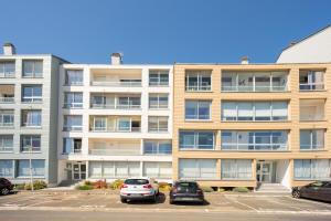 an apartment building with cars parked in a parking lot at Les Vagues in Courseulles-sur-Mer