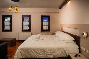 a bedroom with a bed with white sheets and windows at Erofili Hotel & Suites in Portaria