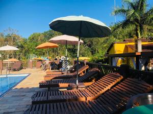 un grupo de bancos con una sombrilla junto a una piscina en Hotel Bosques do Massaguaçu, en Caraguatatuba