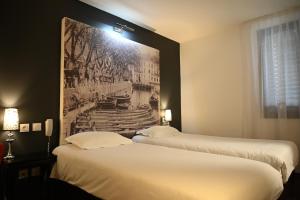 two beds in a hotel room with a picture on the wall at Hôtel Les Muses in Annecy