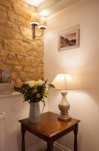 a table with a lamp and a vase of flowers on it at Hook Cottage in Chipping Campden
