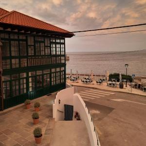 een gebouw naast de oceaan met tafels en stoelen bij Apartamentos El Muelle Comillas in Comillas