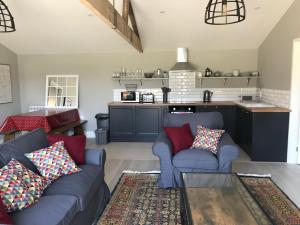 a living room with two blue couches and a kitchen at Glebe Barn, Little Glebe Farm in Cheltenham