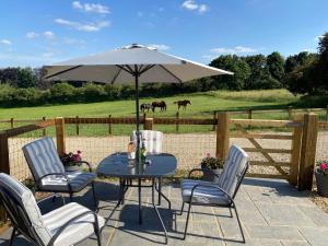 a table and chairs with an umbrella and horses in a field at Glebe Barn, Little Glebe Farm in Cheltenham