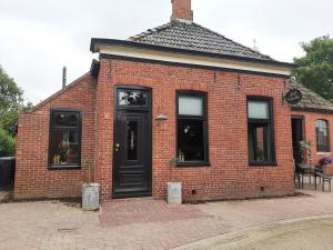 um edifício de tijolos vermelhos com uma porta preta e janelas em De Sarrieshut em Houwerzijl