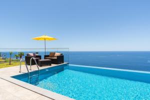 a pool with chairs and an umbrella next to the ocean at Sonho do Oceano in Ribeira Brava
