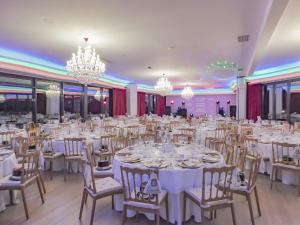 um salão de banquetes com mesas e cadeiras brancas e lustres em Luna Hotel Turismo em Abrantes