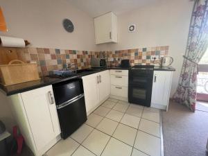 una cucina con armadietti bianchi e lavastoviglie nera di Nethercote Cottage, Kingsize bed, Seven Springs Cottages a Cheltenham
