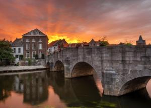 a stone bridge over a river with a sunset at Grand Hotel Valies in Roermond