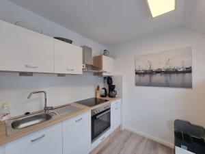 a kitchen with white cabinets and a sink at Ferienwohnung Nordwind in Neßmersiel