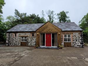 a stone house with a red door in a driveway at Hare Cottage in Ballymena