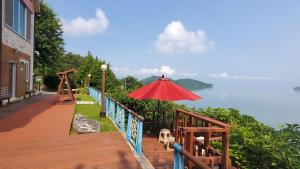 una terraza de madera con sombrilla y vistas al agua en Oh My Family Pension, en Yeosu