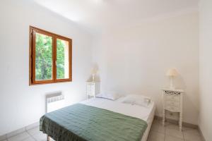 a white bedroom with a bed and a window at La Pinède in Pietrosella