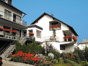ブリーデルにあるWeingut Rosenbaumの白い家のバルコニーに赤い花が咲き誇る