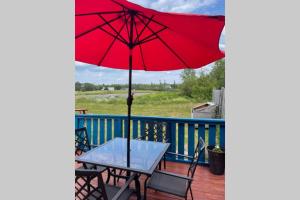 einen Tisch mit einem roten Regenschirm auf dem Deck in der Unterkunft Beautiful 2 Bedroom Apartment in Shediac Bridge in Grande-Digue