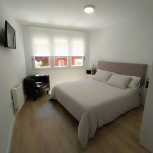 a bedroom with a bed and a chair and two windows at Dúplex Costa de Fisterra I in Finisterre