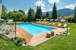 a swimming pool with a wooden deck next to a yard at Tennerhof Luxury Chalets in Kitzbühel