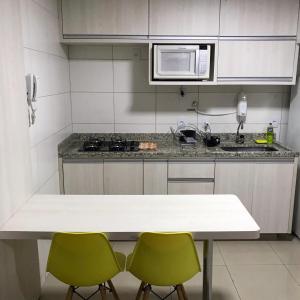 a kitchen with a white counter and two green chairs at Flat The Expression 1210 in Goiânia