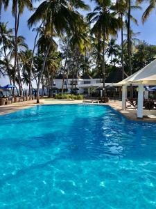 a swimming pool with blue water and palm trees at Kenya Bay Beach Hotel in Bamburi