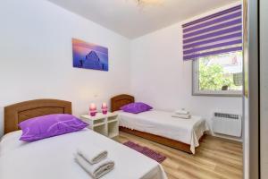 two beds in a room with purple pillows and a window at Casa Verde in Čunski