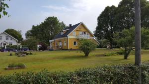 a yellow house on a grassy yard with trees at B&B Parksäter in Håcksvik