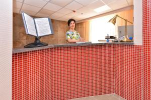 a woman standing behind a red tiled counter with a computer at гостиница Времена года in Sol'-Iletsk