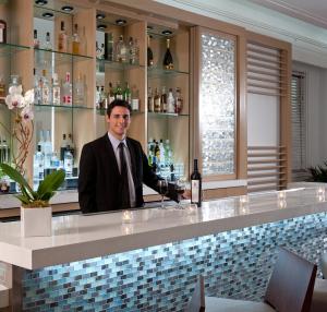 Um homem atrás de um bar a segurar uma garrafa de vinho. em Marseilles Beachfront Hotel em Miami Beach