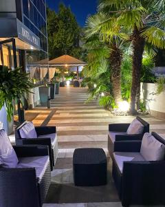 a patio with couches and palm trees in front of a building at Hotel La Perla in Riva del Garda