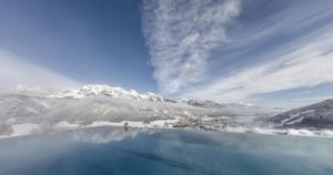 a person standing at the edge of a blue pool with a snow covered mountain at Hotel Schütterhof in Schladming