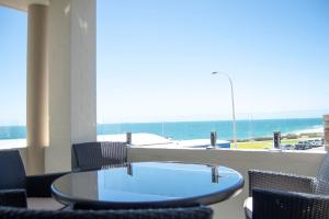 Cottesloe Beach View Apartments #7 في بيرث: طاولة زجاجية مع كراسي وإطلالة على المحيط