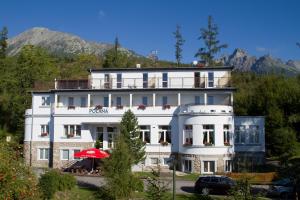 a large white building with mountains in the background at Penzión Poľana in Starý Smokovec