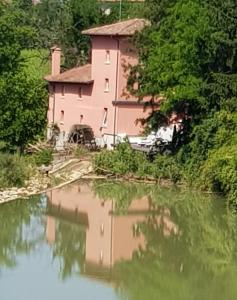 Mulino dell'Abbazia Country Resort في Corno di Rosazzo: مبنى وردي بجانب جسم ماء