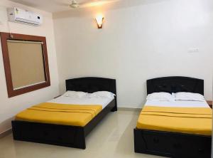 two beds in a room with yellow sheets and a mirror at Orchid Home in Bengaluru