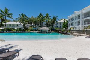uma piscina de resort com cadeiras e palmeiras em Beach Club Palm Cove 2 Bedroom Luxury Penthouse em Palm Cove