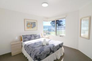 a white bedroom with a bed and a window at Pelican Waters in Merimbula