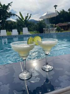 two martini glasses sitting on a table next to a swimming pool at Hotel Campestre Campos Verdes in Roldanillo