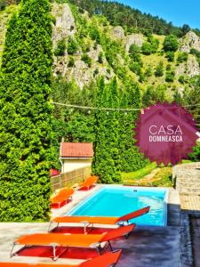 a swimming pool with orange chairs and a mountain at Casa Domneasca in Baia de Fier