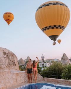 a man and woman standing next to a pool with hot air balloons at Cappadocia Caves Hotel in Göreme